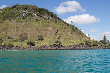 Naklejka premium Beautiful Burleigh Headland Covered In Lush Green Grass Surrounded By Turquoise Ocean Water View From Behind A Fishing Boat