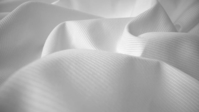 Shiny flowing cloth texture dolly shot in close up view macro shot. Wavy clean silk weave material. Textile abstract background. Bed sheet, curtain and clothing industry concept.