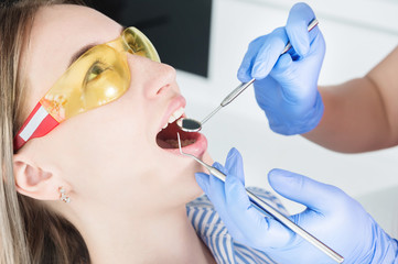 A close-up of the girl's face is examined by a dental examiner with his mouth open and a napkin and eyes closed. Dentist hands with inspection tools