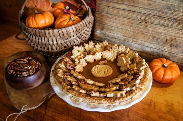 Homemade Pumpkin Pie Decorated with Pastry Cutouts of Autumn leaves with a center pumpkin, set on a wooden board with fresh pumpkins and pecans, selective focus