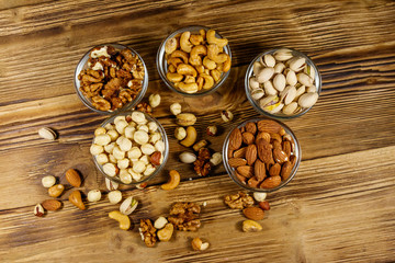 Assortment of nuts on wooden table. Almond, hazelnut, pistachio, walnut and cashew in glass bowls. Top view. Healthy eating concept