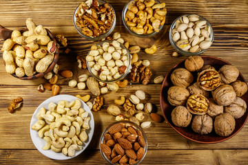 Assortment of nuts on wooden table. Almond, hazelnut, pistachio, peanut, walnut and cashew in small bowls. Top view. Healthy eating concept