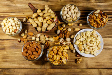 Assortment of nuts on wooden table. Almond, hazelnut, pistachio, peanut, walnut and cashew in small bowls. Top view. Healthy eating concept