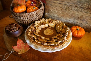 Homemade Pumpkin Pie Decorated with Pastry Cutouts of Autumn leaves with a center pumpkin, set on a wooden board with fresh pumpkins and pecans, selective focus