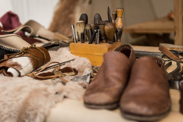 Shoemaker working desk with set of tools, ready shoes foreground and material background, selective focus