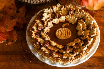 Homemade Pumpkin Pie Decorated with Pastry Cutouts of Autumn leaves with a center pumpkin, set on a wooden board with fresh pumpkins and pecans, selective focus