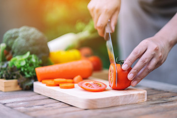 Closeup image of a woman cutting and chopping tomato by knife on wooden board
