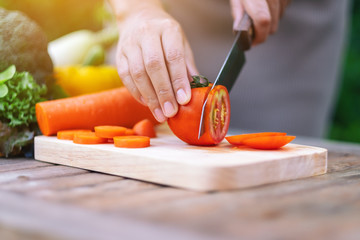 Closeup image of a woman cutting and chopping tomato by knife on wooden board