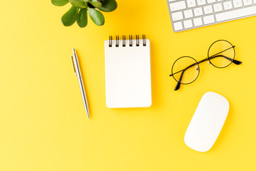 Business background with empty notebook on yellow table. Office desktop with accessories