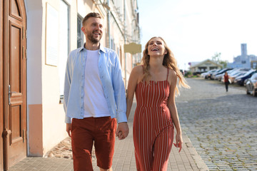 Beautiful young couple holding hands and smiling while walking through the city street