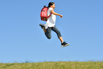 青空でジャンプする小学生の女の子（ランドセル）