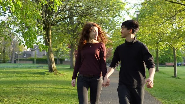 Gimbal Follow Shot of Young Energetic Mixed Ethnicity Couple Holding Hands and Walking Together in Park