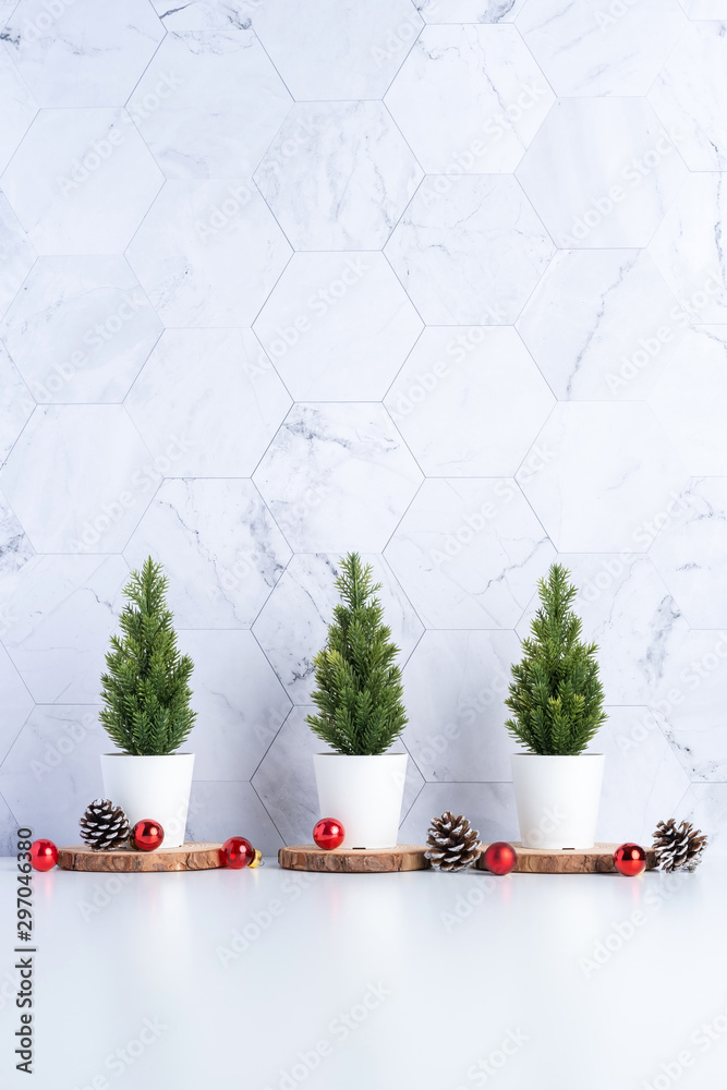 Poster Three christmas tree with pine cone and decor xmas ball on white table and marble tile wall background.clean minimal simple style.holiday still life mockup banner with space to adding text