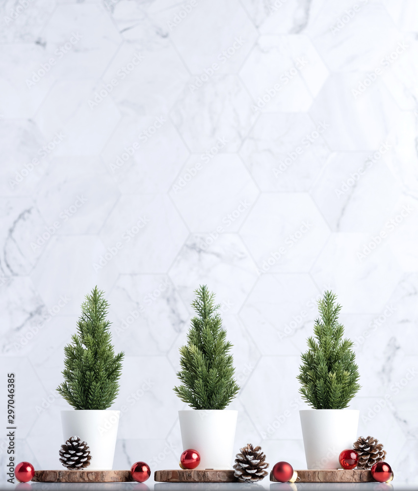 Poster Three christmas tree with pine cone and decor xmas ball on white table and marble tile wall background.clean minimal simple style.holiday still life mockup banner with space to adding text