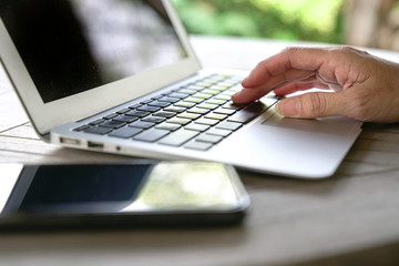 Hands typing on the keyboard of a laptop with cell phone next to it.