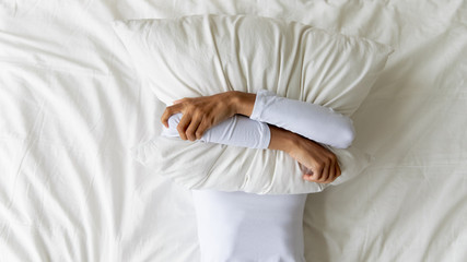 Young girl lying on bed, covering face with pillow.