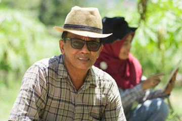 modern farming concept, old asian male farmer sit at papaya farm
