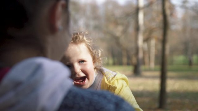 Young mother entertains her fair-haired curly  lovely baby girl in autumn park. Cheerful mood, positive emotions, happy childhood. Having fun. Family portrait, sun flares. Slow motion.