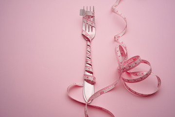 Fork and spoon tied with a pink measuring tape on a pink background : healthy diet concept.