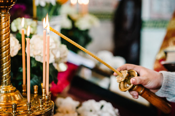 The priest's hand lights a candle near the candlestick in the church.