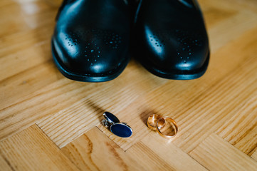 Part stylish men black shoes, cufflinks, wedding two rings lying on a light brown table. Wedding accessories groom on rustic wooden background. idea composition.