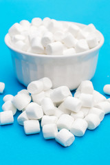 Fototapeta na wymiar Heap of small marshmallow with full bowl of small marshmallow on blue.