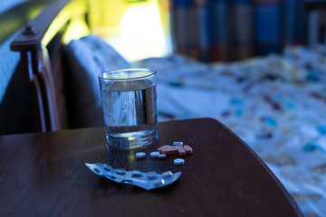 some of medicine pills and a glass of water  on a nightstand next to the bed at night, treatment insomnia concept