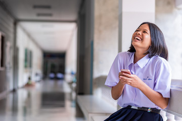 Smiling Asian female high school student in white uniform is enjoying social media on her smartphone.