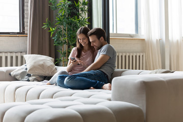 Happy couple in love relaxing on couch, using phone together