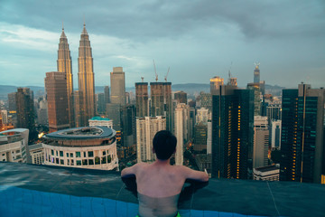 guy in pool from behind looking at skyscrapers