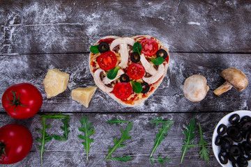 Heart shaped pizza ingredients. The name of the pizza is written in arugula.