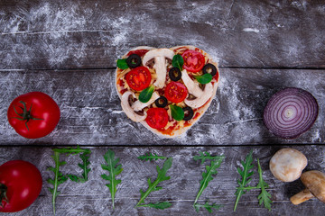 Heart shaped pizza ingredients. The name of the pizza is written in arugula.
