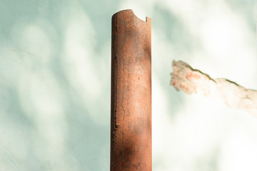 Broken and rusted metal pipe on a wall background with shadows from tree leaves