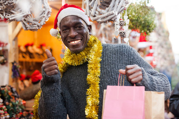 Smiling man in Santa hat with shopping bags on Christmas fair