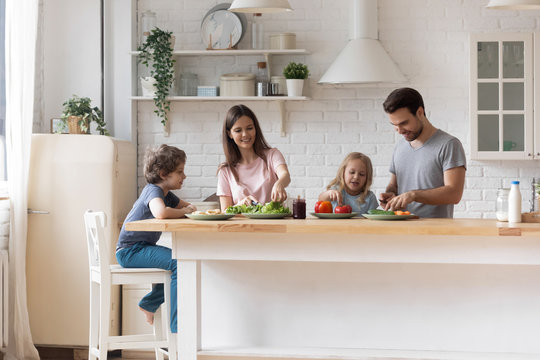 Happy family with little children preparing salad together