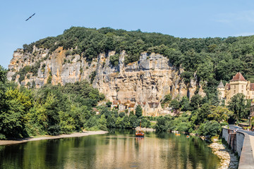 Fototapeta na wymiar La Roque Gageac, one of France's most beautiful villages by the Dordogne River, backed by a steep hill / cliff, Malartrie Castle in the background. Canoeing on the river. Travel France.