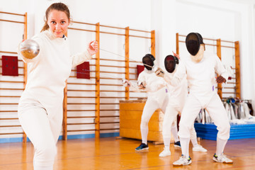Young female fencer practicing fencing technique in training room