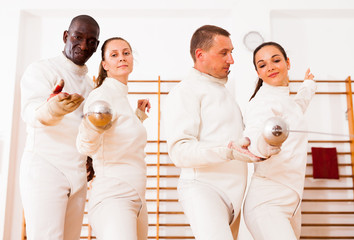 Smiling fencers posing with foils  together at fencing room