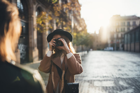 Blogger photoshoot concept. Photographer with camera take photo model girlfriend. Tourist smiling girl travels in Barcelona holiday with traveler friend. Sunlight flare street in europe city