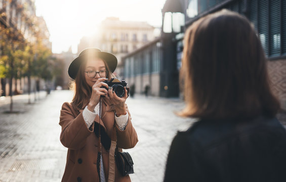 Photographer with camera take photo model girlfriend in europe city. Blogger photoshoot concept. Tourist smiling girl travels in Barcelona holiday with traveler friend. Sunlight flare street
