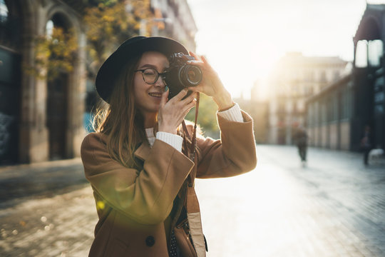 Photographer with retro photo camera. Tourist portrait. Girl in hat travels in Barcelona holiday. Sunlight flare street in europe city. Traveler hipster shooting architecture, copy space mockup