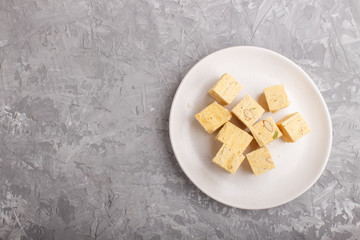 traditional indian candy soan papdi in white plate with almond and pistache on a gray concrete background. top view
