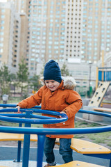 Little boy 5 years old in an orange jacket at the playground. Children's leisure outdoors, games on the street.