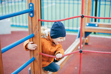 Fototapeta premium Little boy 5 years old in an orange jacket at the playground. Children's leisure outdoors, games on the street.