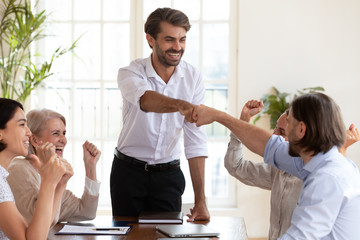 Obraz premium Excited businessmen fist bumping at meeting celebrating corporate teamwork success