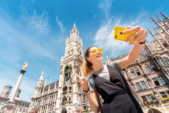 Cheerful Asian tourist girl takes a selfie on the background of Munich attractions to post photos on her blog and social networks