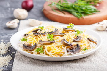 Rice noodles with champignons mushrooms, egg sauce and oregano on a black concrete background. side view, selective focus.