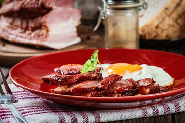 Slices of smoked bacon and fried egg on a red plate