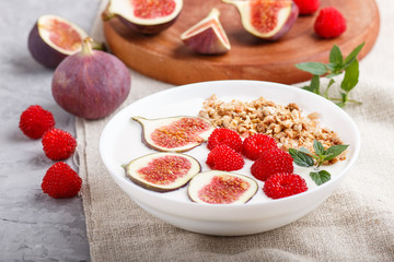 Yoghurt with raspberry, granola and figs in white plate on a gray concrete background and linen textile. side view, selective focus.