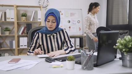 beautiful islam woman accountant working with computer and counting calculator. elegant asian chinese coworker walking back to seat in modern office. diverse young people worker employee workplace.